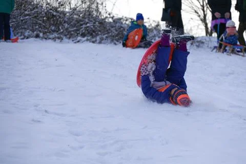 Child falling while sledding downhill on snowy hill during winter activity Stock Photos