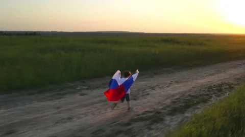 A child in a field with a Russian flag at sunset. Evening light . Summer Video stock 156448434