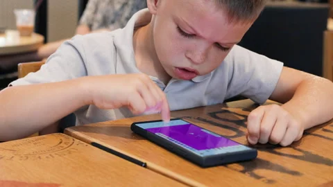 Child focused on creating digital art with stylus on smartphone at cozy cafe. Stock Footage 287985678