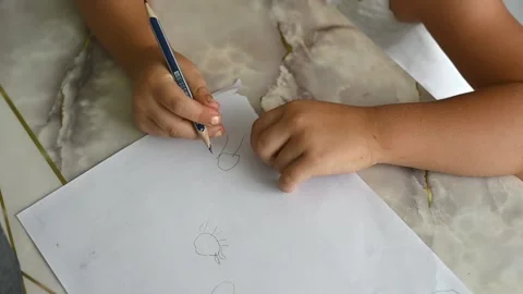 Child focused on drawing with pencil on white paper, creating basic shapes like 스톡 동영상 330156285