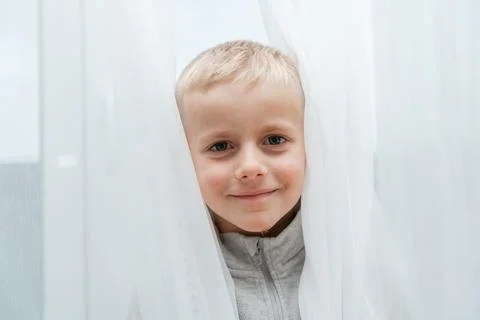 Child framed by translucent drapery, smiling directly at camera, soft tones and Fotos de archivo