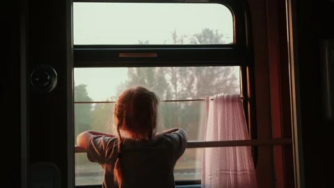 Child gazes out of a train window during golden hour, capturing a moment of Stock Footage 318289444