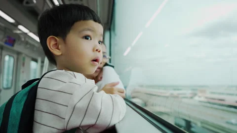 Child gazing out window of train while holding bottle, observing scenery on a Stock Footage 300003442