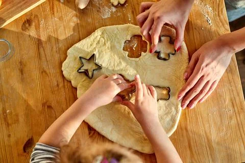 Child girl baking cookies with mum, rolls out the dough and uses moulds to make Stock Photos