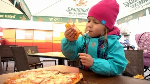 Child girl eating a Pizza by Hands while sitting on a cozy Cafe Table Stock Footage