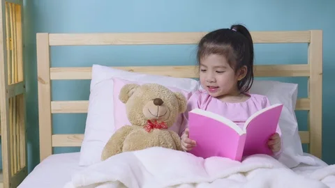 Child girl reading a book with her teddy bear on the wooden bed Stock Footage 104842453
