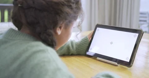 Child girl sitting at table by window reaching, lifting tablet, tapping screen, Stock Footage 341467320