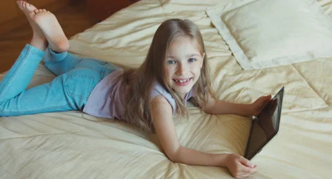 Child girl using tablet pc lying on the bed and smiling at camera. Top view Stock Footage 55882756