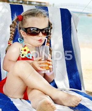 Child in glasses and red bikini drink juice. Stock Photos