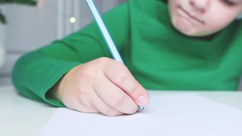 A child in green clothes sitting at the table writes a letter, a close-up Stock Footage 165384022