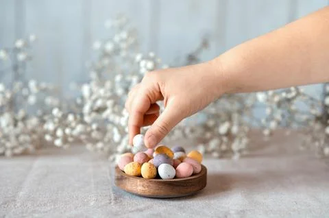 Child hand picking easter chocolate Multi-Colored eggs from wooden bowl with Stock Photos