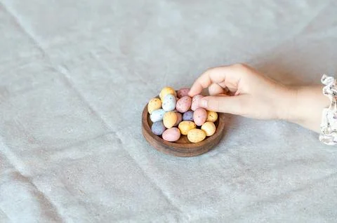 Child hand picking easter chocolate pastel colors eggs from wooden bowl. Top Stock Photos