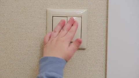 Child hand pressing light switch on wall. Small kid turning off electric lamp Stock Photos