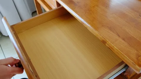 Child hand pulls open a wooden desk drawer using a round knob in a close-up Stockbeeldmateriaal 330477316