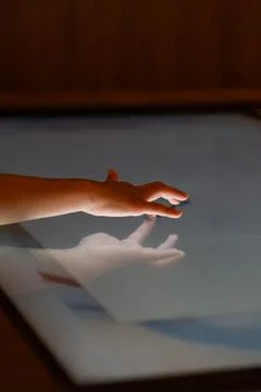 Child hand touching an illuminated interactive surface with reflection repr.. Stock Photos