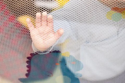 Child hand touching mesh from inside playpen Stock Photos