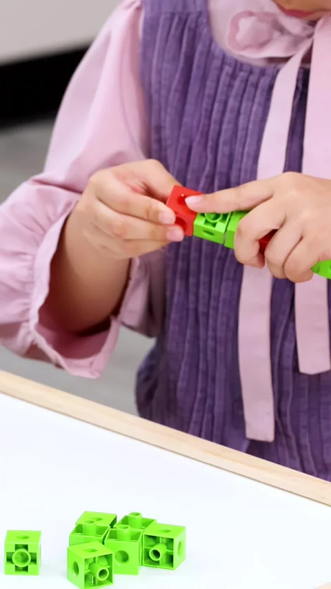 Child Hands Assembling Red and Green Interlocking Cubes on White Table Video stock 324935294