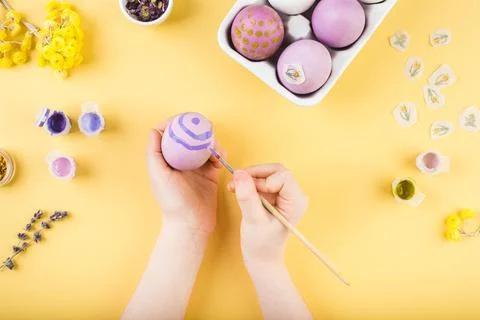 Child hands decorate Easter eggs on yellow background. Happy easter concept. Stock Photos
