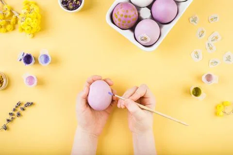 Child hands decorate Easter eggs on yellow background. Happy easter concept. Stock Photos