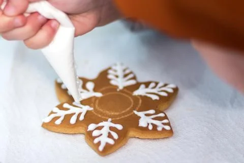 Child hands decorating gingerbread in the form of a a snowflake with icing su Stock Photos