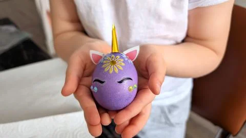 Child Hands Gently Holding Creative Unicorn Decorated Purple Egg At Home Stock Photos