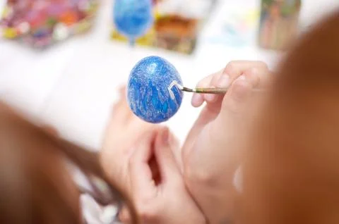 Child hands painting blue easter egg with white lines Stock Photos