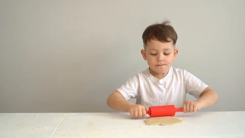 Child hands rolling dough with a rolling pin. Boy rolls out the dough on the Video stock 128827244