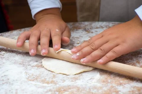 Child hands rolling dough with rolling pin on wooden table Stock Photos