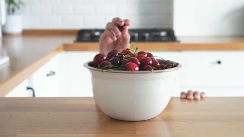 Child hands takes the sweet cherry from the bowl on wooden table Stock Footage 246008076