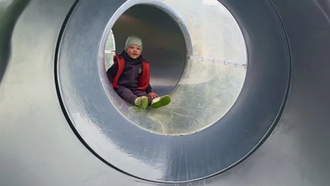 The child is happily crawling through the slide tunnel on the playground. Kid Stock Footage 247968012
