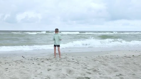 A Child is Happily Exploring the Beach Waves on a Cloudy and Overcast Day Stock Footage 315863771
