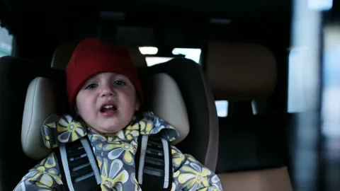 Child in hat and jacket waves hands and screams in car Stock Footage 154398482