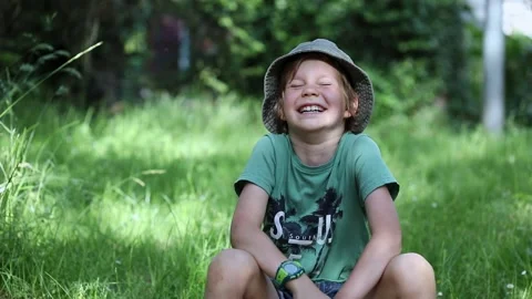 A child in hat sits on the grass and laughs Stock Footage 157236980