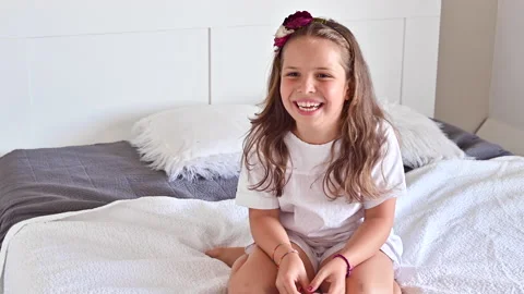 The child is having fun on the bed, jumping and laughing. Little girl in pajamas Stock Footage 138232290