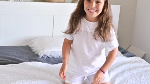 The child is having fun on the bed, jumping and laughing. Little girl in pajamas Vidéo 138234281