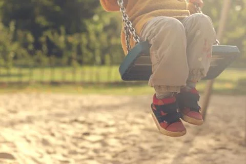 Child having fun with swing on a playground in bright afternoon sun Stock Photos