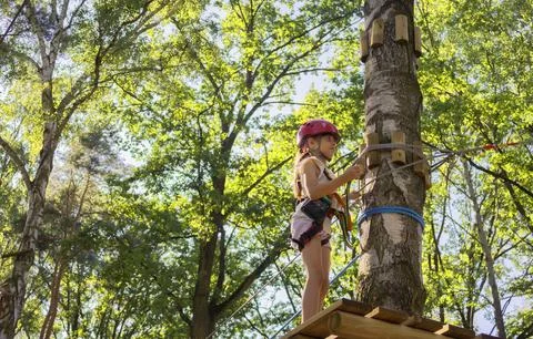 Child in helmet navigating tree climbing obstacle course in summer Stock Photos