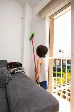 Child helping cleaning home using broom in living room Foto stock