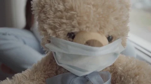 A child with her teddy bear both in masks stay by the window in the room Stock Footage 127579398