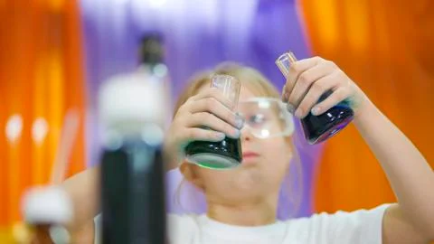 Child is holding flasks of colored liquid. Cute girl in protective transparent Stock Photos