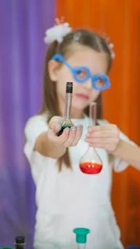 Child is holding flasks of colored liquid. Cute girl with blue round glasses on Stock Photos