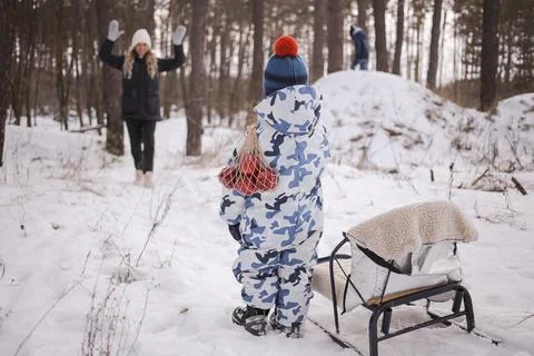 A child holds a string bag with apples in his hands, standing near the sled Stock Photos