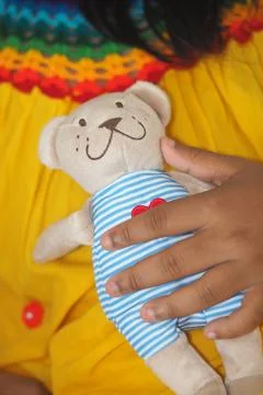Child holds a teddy bear while wearing a colorful dress Stock Photos