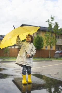 A child holds a yellow umbrella standing in a puddle outside. On sunny day happy Stock Photos