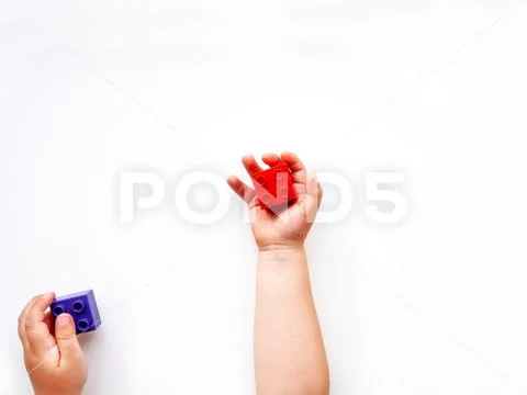 Child is holidng violet and red constructor blocks in fists. Kid's hands with Stock Photos