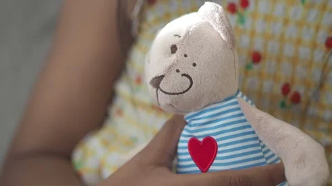 Child hugs a soft teddy bear with a heart patch Vídeos de archivo 320659940