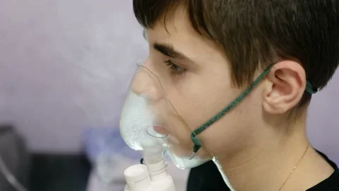 Child inhale using a nebulizer. 13-year-old boy in a nebulizer mask close up Stock Footage 145708820