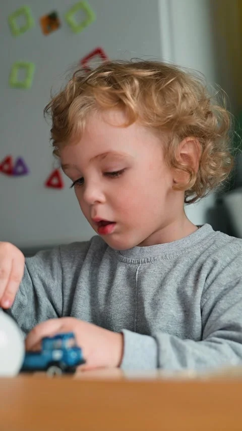 A child interacts with a small toy car and a white object while seated at a Stockbeeldmateriaal 337112560