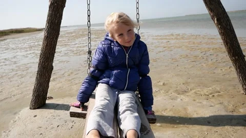 A child in a jacket is riding a swing on a warm autumn day on the seashore. Vídeos de archivo 142590205