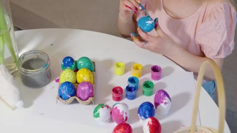 A child joyfully colors Easter eggs using various vibrant paints Stock Footage 302043923